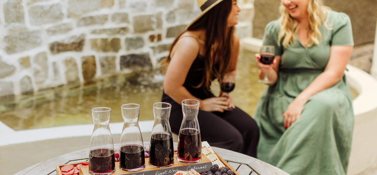 two women having a glass of wine and chatting with a wine sampler and snacks sitting on a table near them