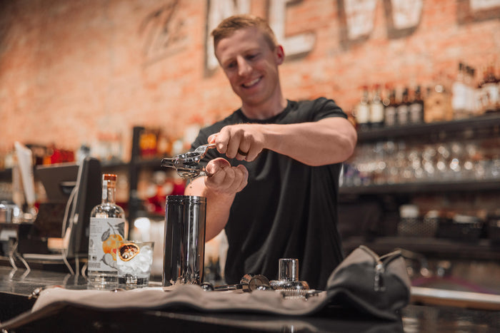 A man skillfully prepares a cocktail at a bar, surrounded by various bottles and bar tools.