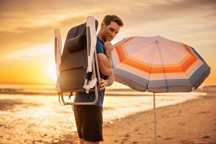 A man walks along the beach, holding an umbrella against the wind and sun.
